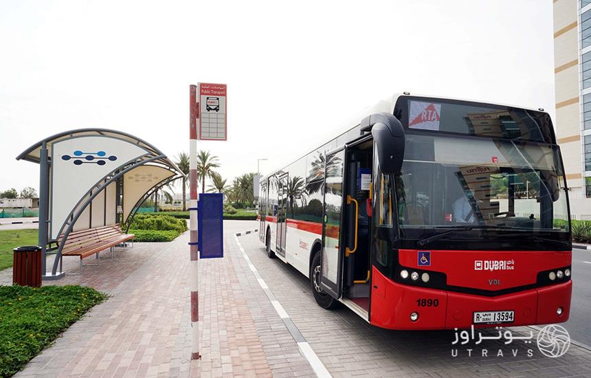 اتوبوس قرمزرنگ متعلق به شرکت اتوبوس‌رانی دبی، توقف کرده مقابل ایستگاه